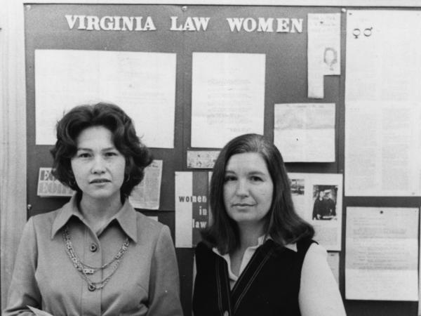 Two women stand in front of a bulletin board displaying Law Women materials