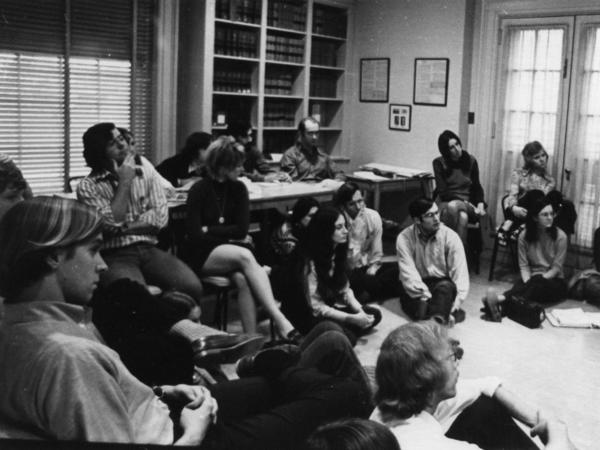 A group of students sit and listen to a speaker out of frame. 