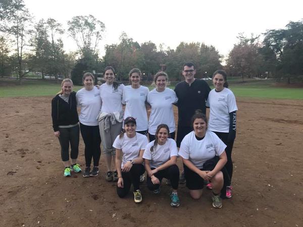 Color photograph of group of smiling men and women on softball pitch