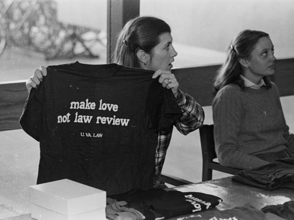 Black and white photograph of two women tabling. One woman holds a t-shirt which reads: "make love not law review."