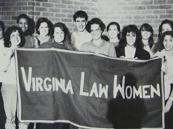Black and white photograph of group of people smiling and holding banner which reads "Virginia Law Women"